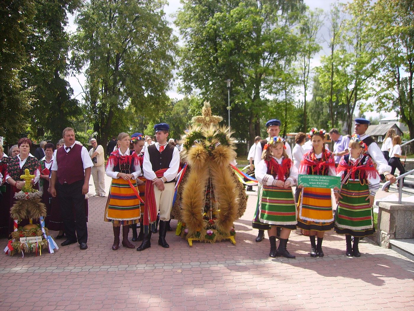 Villagers in traditional dress presenting tall dozynki harvest wreaths of woven grain